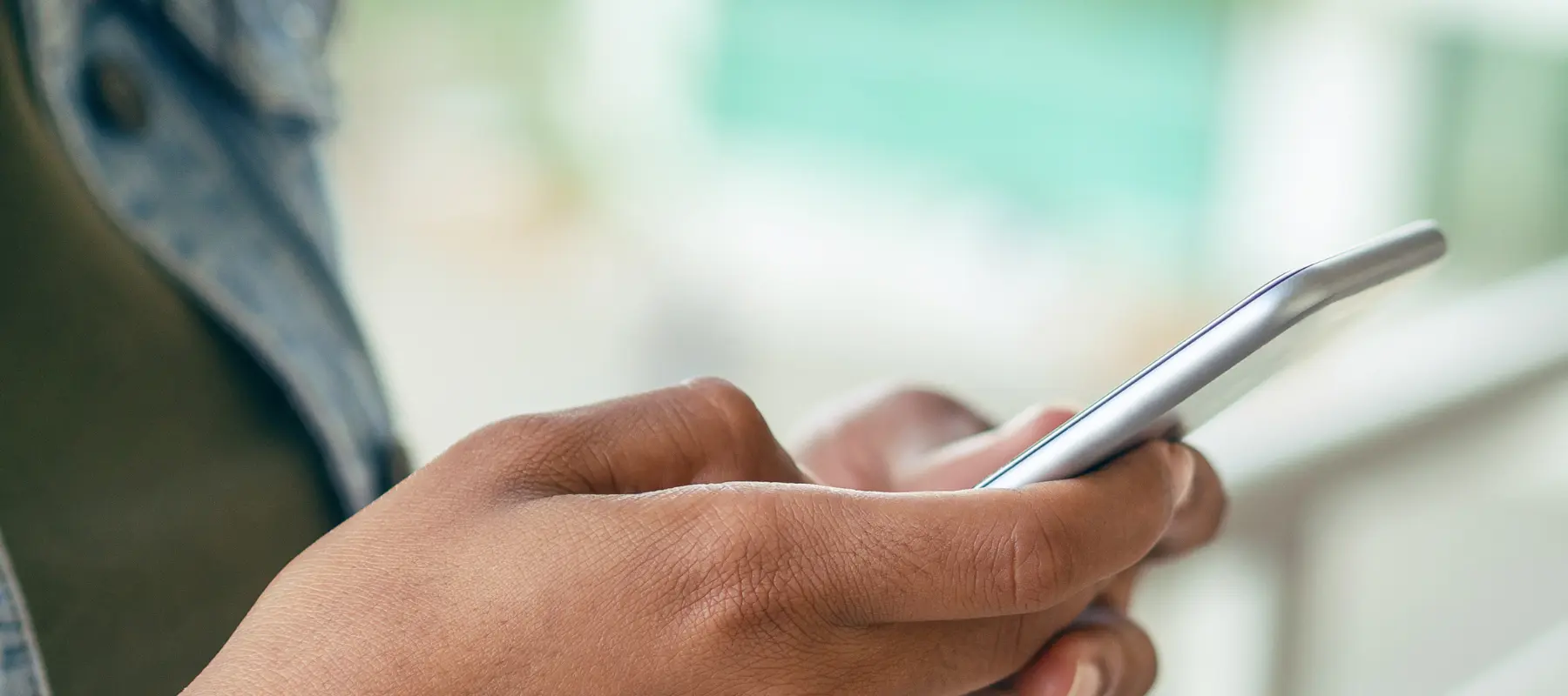 Close-up of a person holding a smartphone and using their thumbs to type on the screen, with a blurred background.